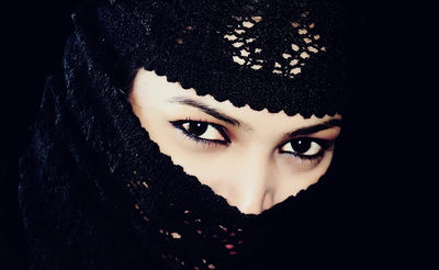 A striking close-up portrait featuring a woman with her face partially covered by a black lace veil, revealing only her expressive eyes. The dramatic contrast and dark background create a mysterious, captivating image perfect for artistic and conceptual t