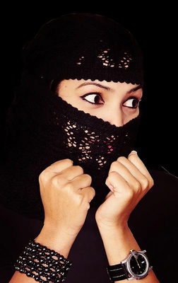 A striking portrait of a woman partially covering her face with a black lace veil, revealing a wide, expressive gaze. Her hands frame the veil while dark accessories add contrast, creating a bold, emotive image perfect for artistic and conceptual photogra